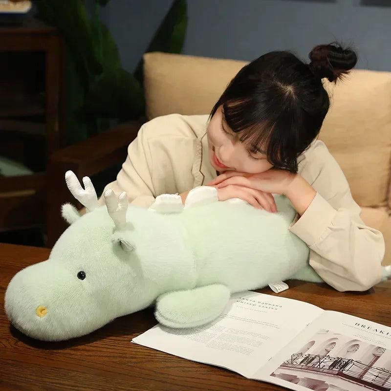 Person holding a large green kawaii plush dragon toy on a table with a magazine underneath.