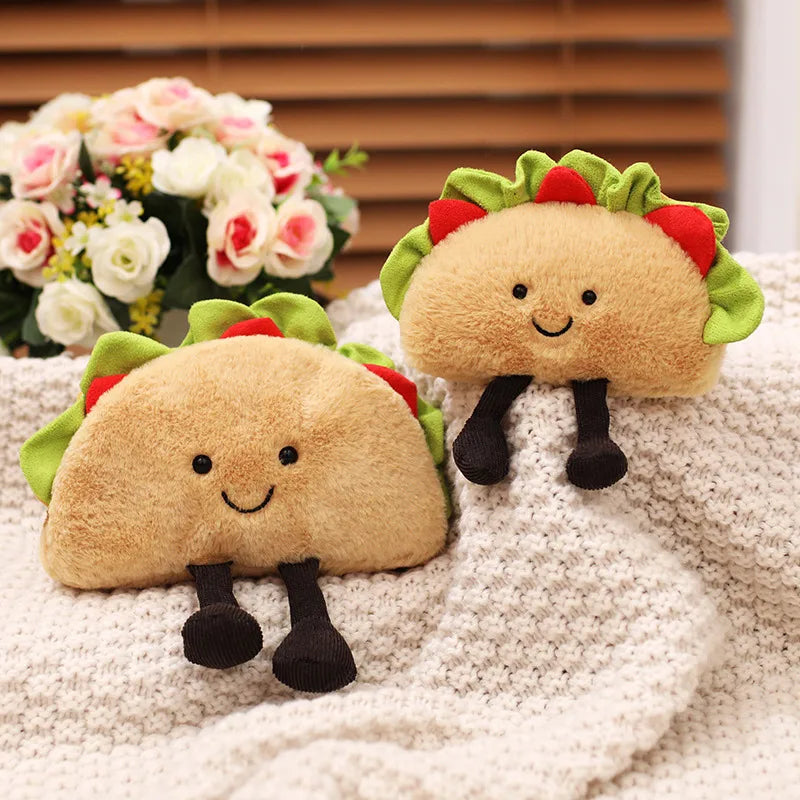 Two kawaii plush taco toys on a textured surface with flowers in the background