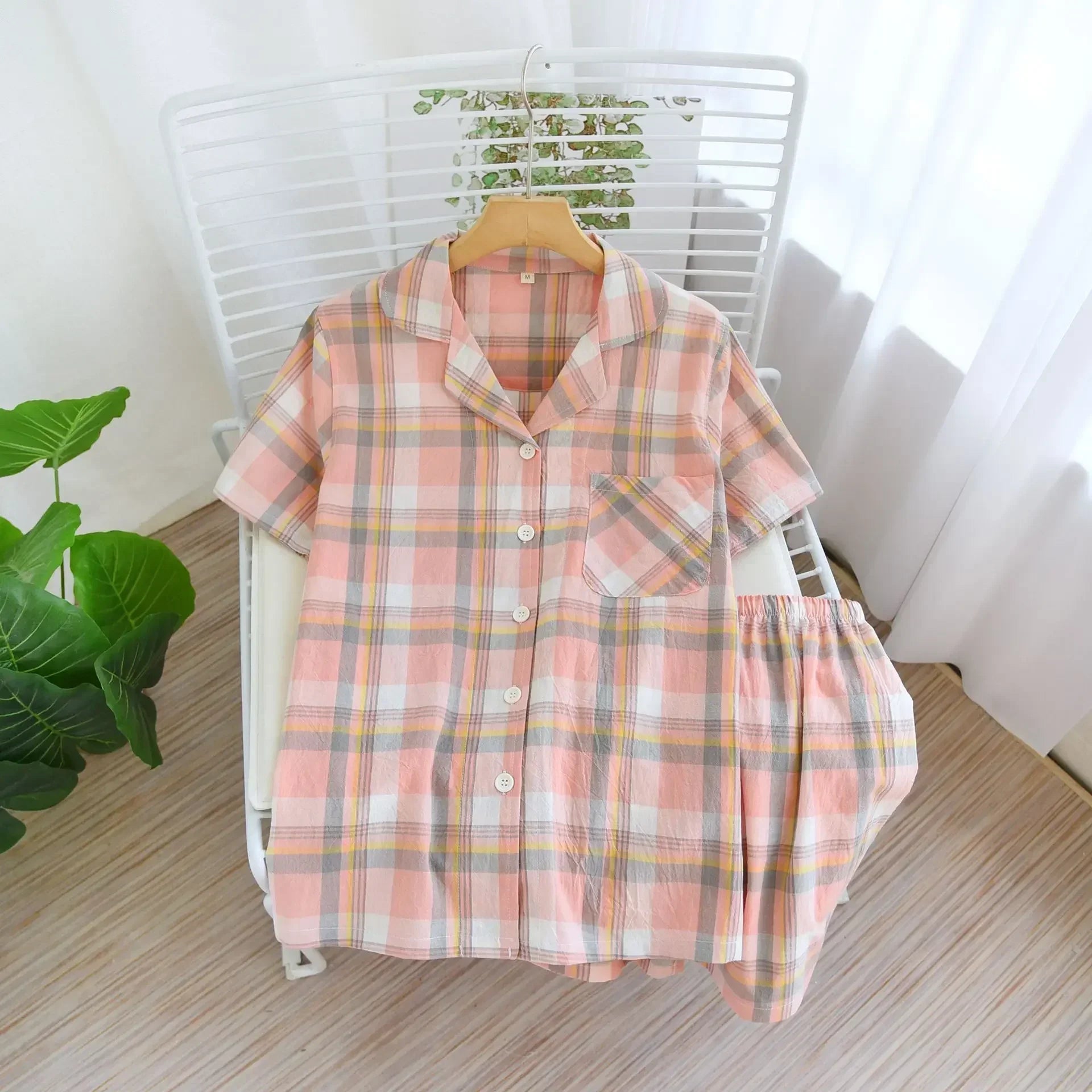 Pink kawaii plaid shirt on a hanger with a white chair and plant in the background