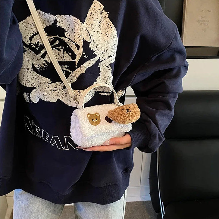 Person wearing a dark blue hoodie with a graphic design, holding a small plush bag with a Kawaii bear design.