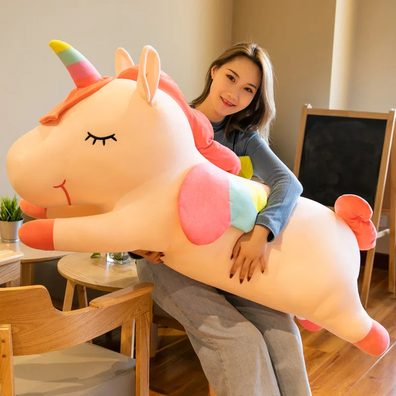 Woman sitting on a large, colorful unicorn plush kawaii toy in a room with wooden furniture.