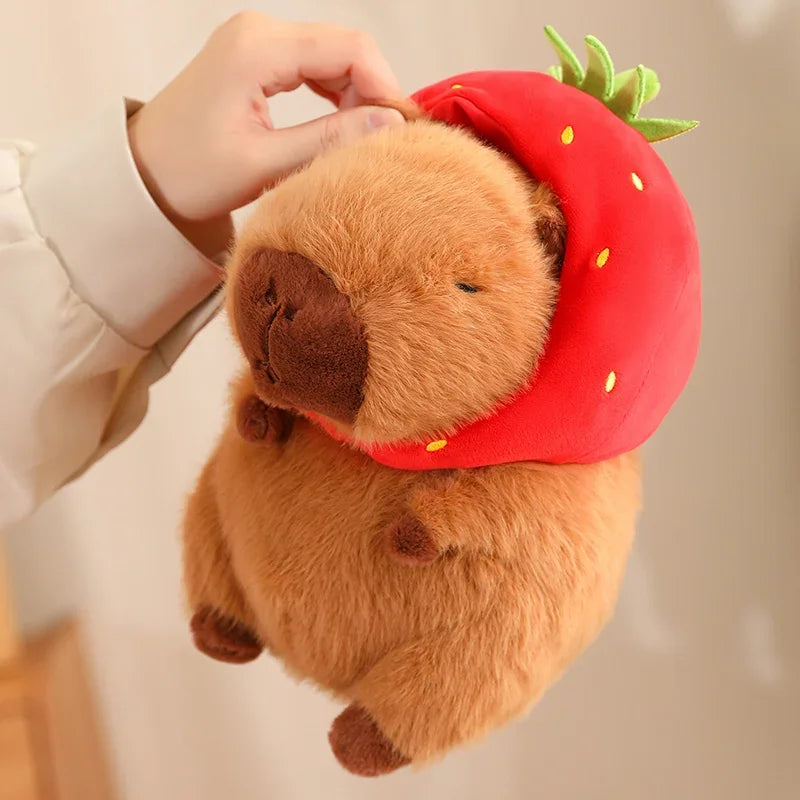 Kawaii plush toy bear wearing a strawberry hat held by a person against a neutral background