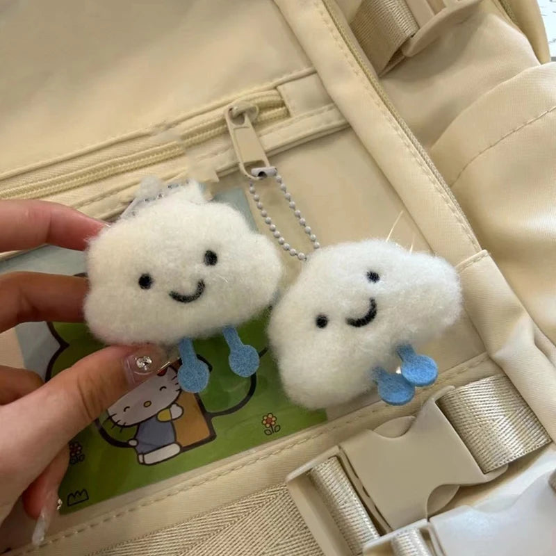 Two kawaii fluffy cloud-shaped keychains with smiling faces held over a beige bag.