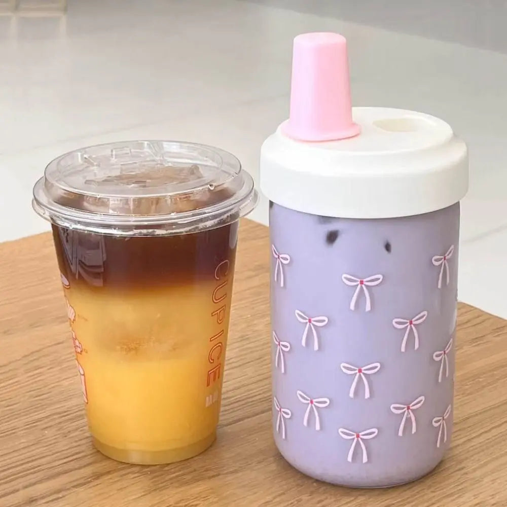 Clear Kawaii cup with iced drink and purple sippy cup with pink lid on a wooden surface
