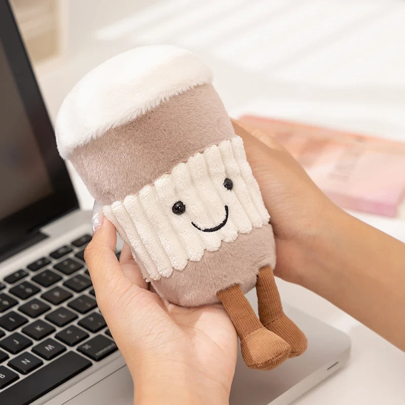 Plush kawaii toy resembling a marshmallow with a smiley face held by a hand in front of a laptop.