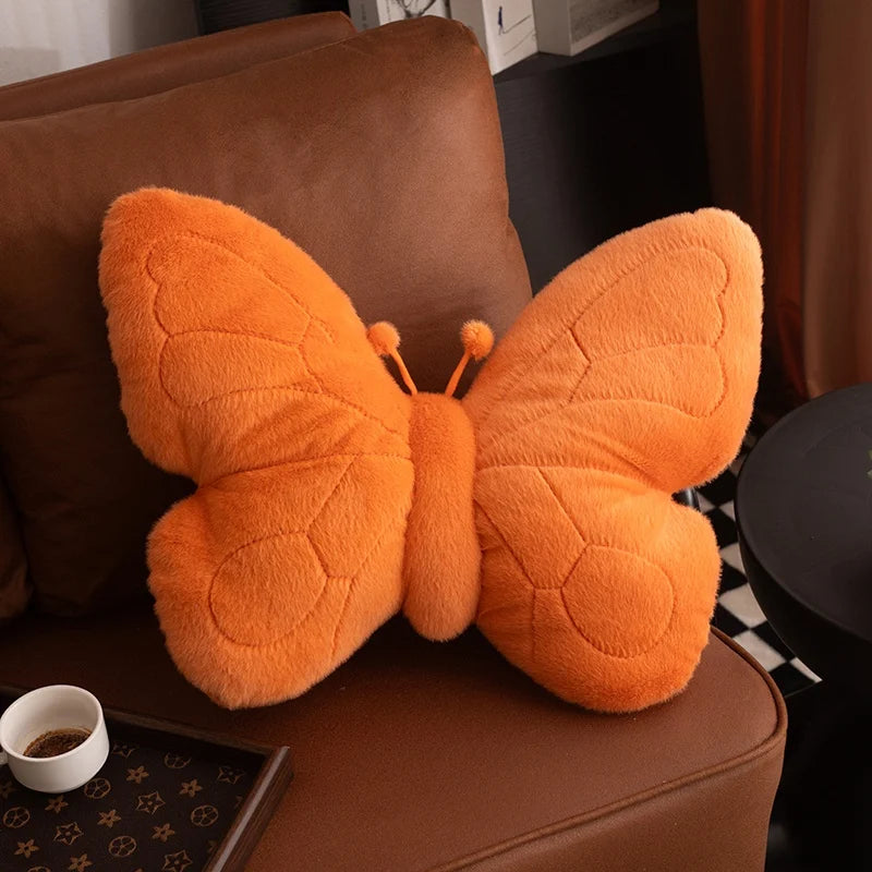 Orange butterfly-shaped kawaii pillow on a brown couch with a cup and tray in the background.