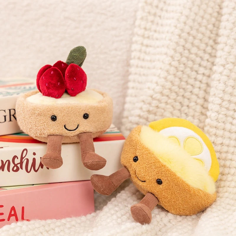 Two kawaii plush toys resembling a cake and a lemon on a textured surface with books in the background.