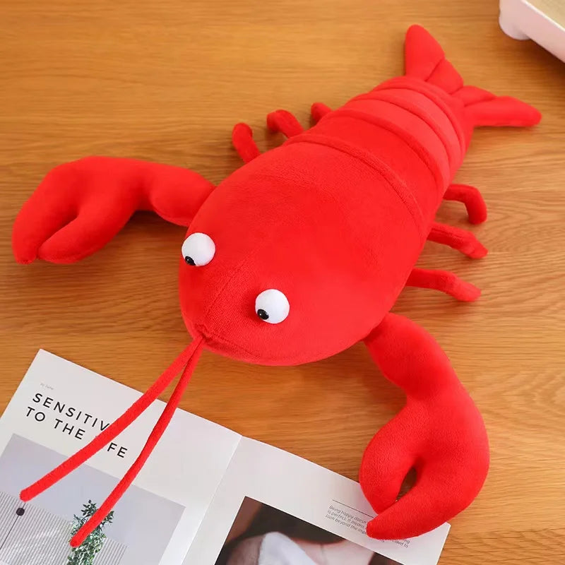 Red kawaii plush lobster toy on a wooden surface with a magazine underneath