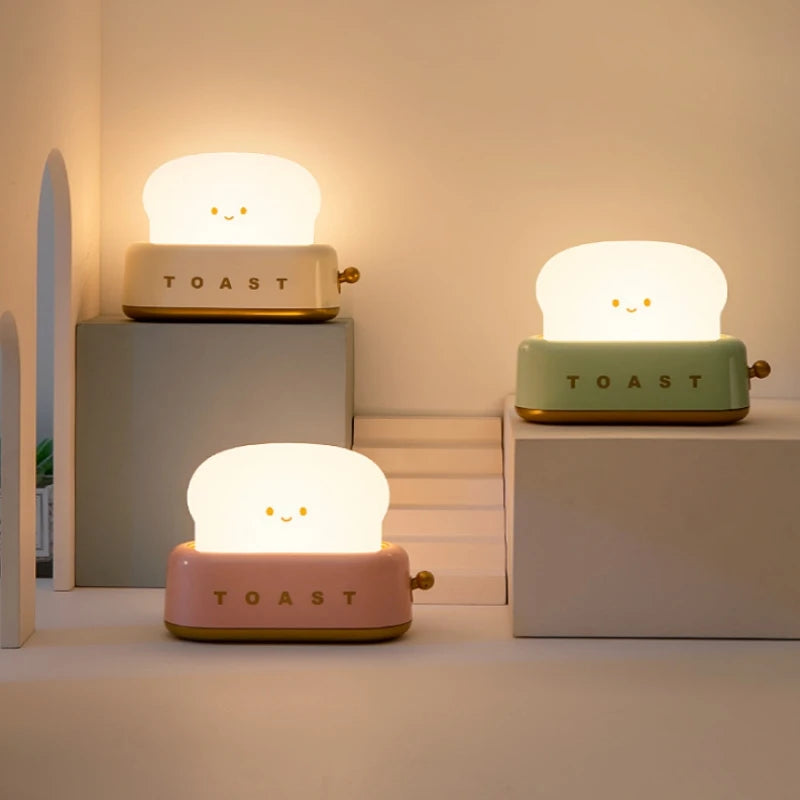 Three cute toast-shaped kawaii night lights in different colors on a neutral background.