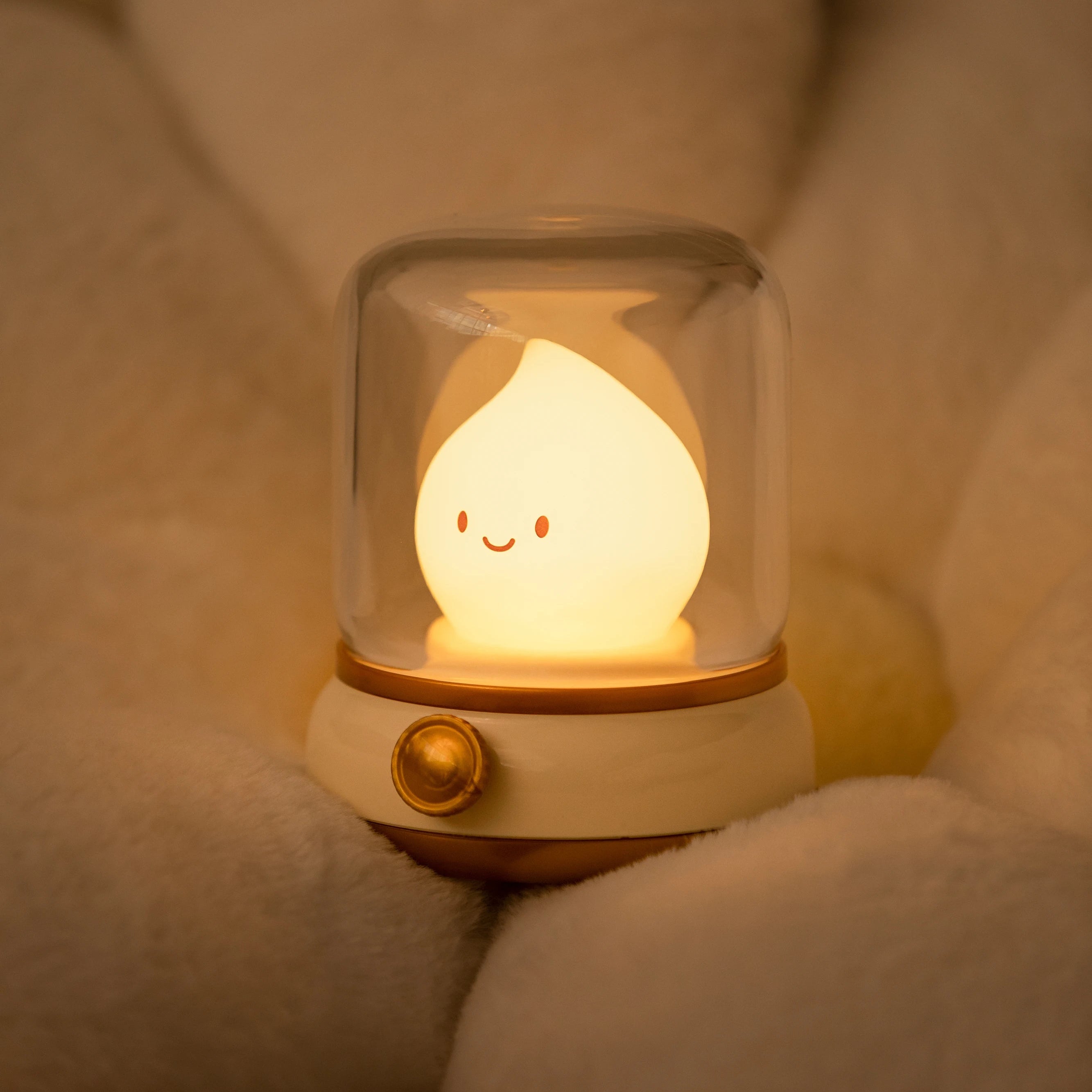 Cute kawaii night light with a smiling face inside a glass dome on soft white fabric.