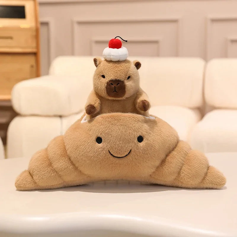 Kawaii plush toy shaped like a croissant with a small plush animal on top, sitting on a light-colored couch.