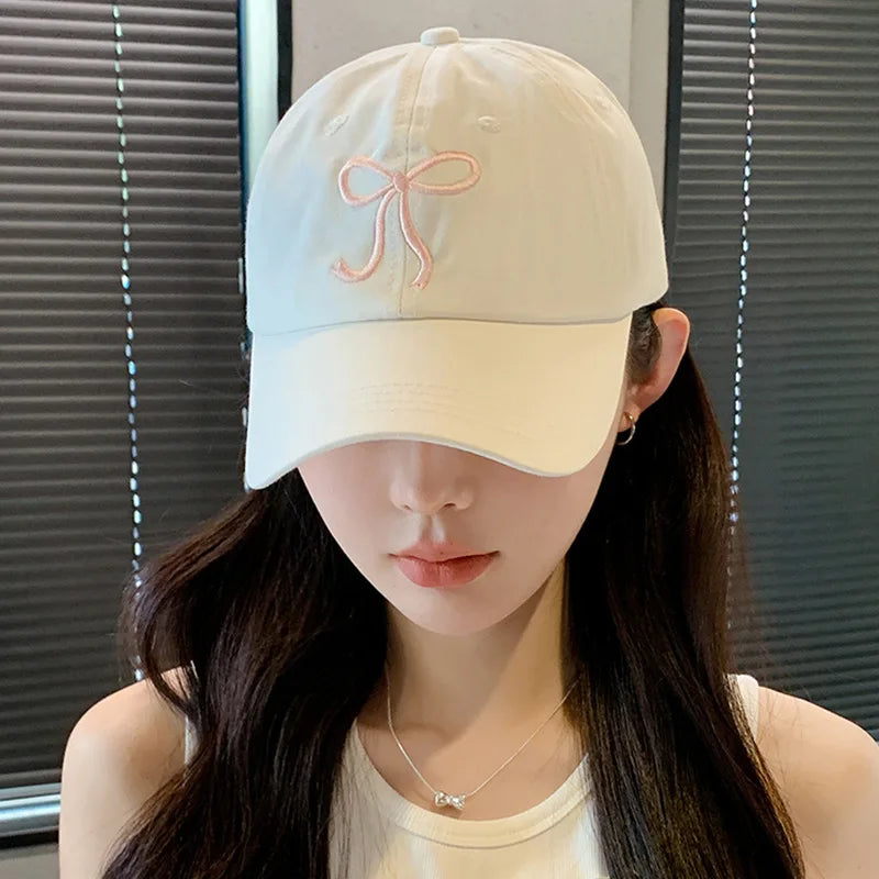 Person wearing a light-colored Kawaii baseball cap with a pink bow design against a neutral background