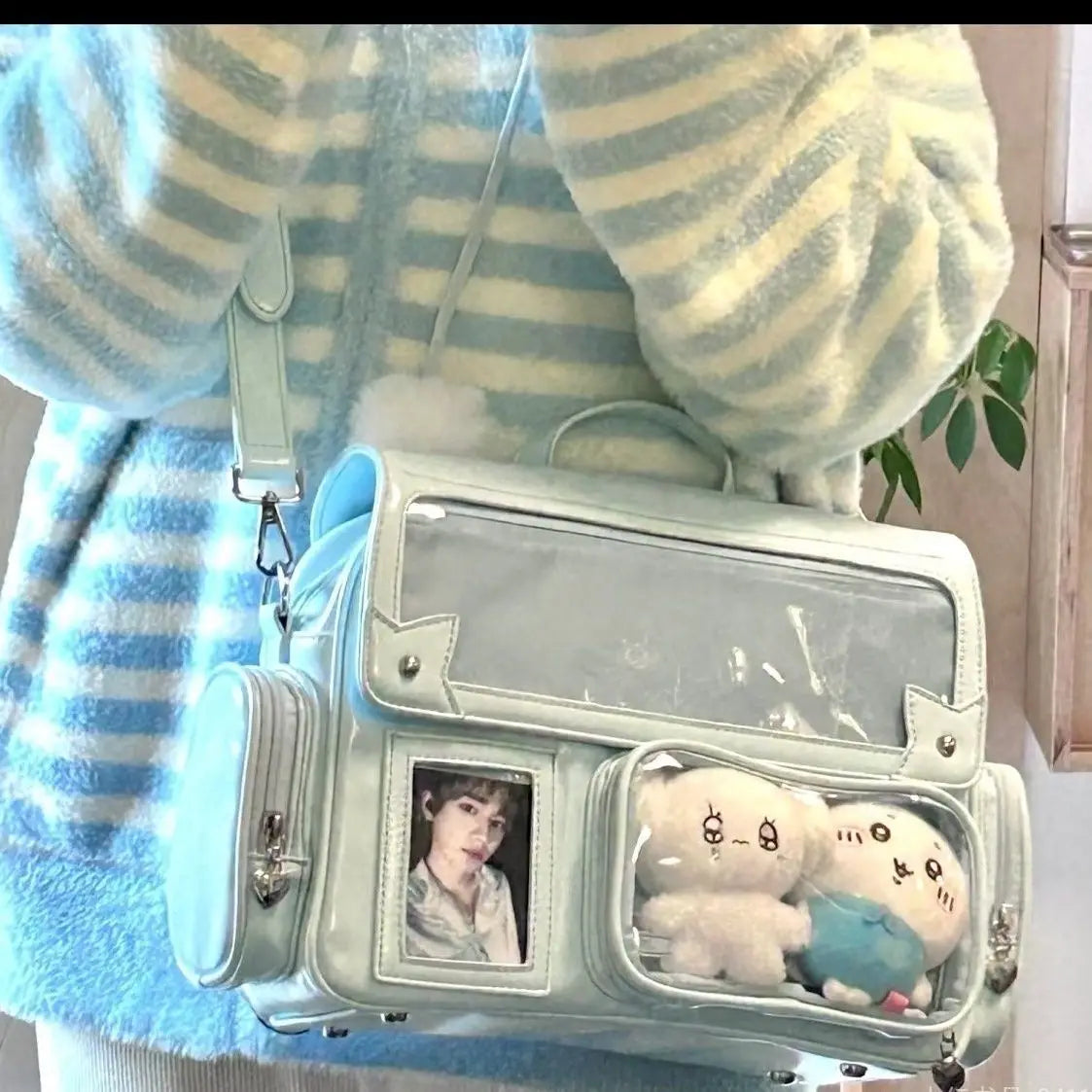 Clear handbag with small Kawaii plush toys and a photo inside, worn by a person in a striped sweater.