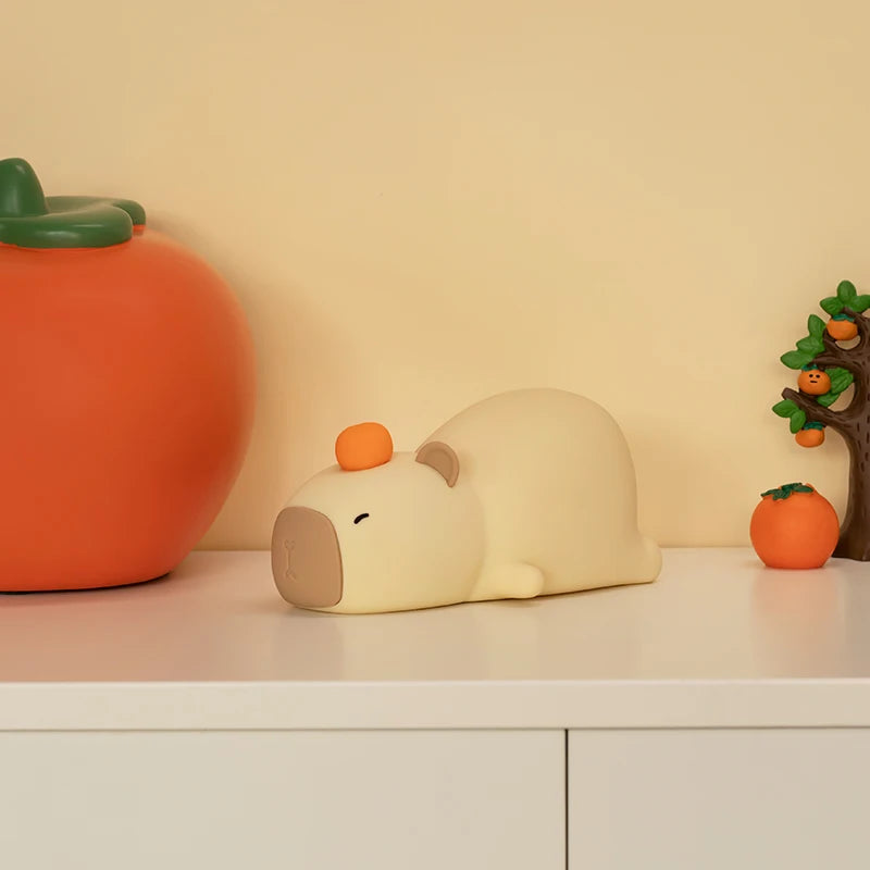 Decorative items including a large orange pumpkin, a small white kawaii bear-like figure with an orange on its head, and a tree with small orange fruits on a light-colored surface.