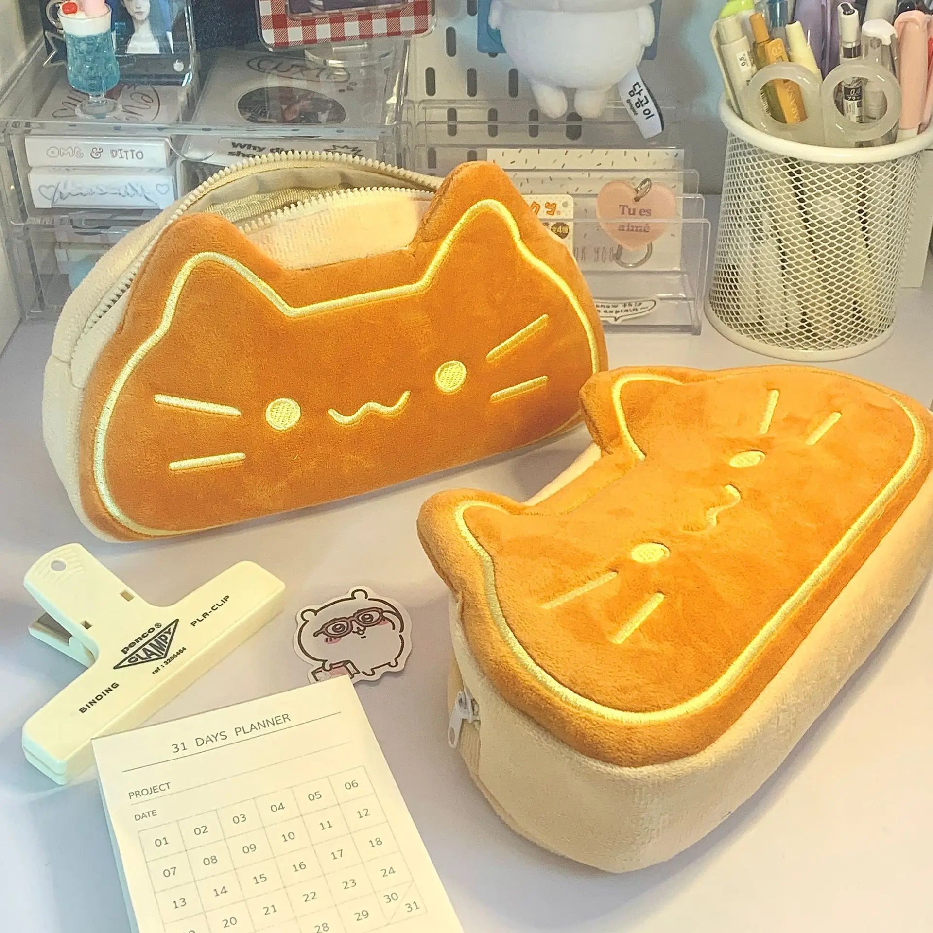 Two cat-shaped kawaii orange pouches on a desk with stationery items.