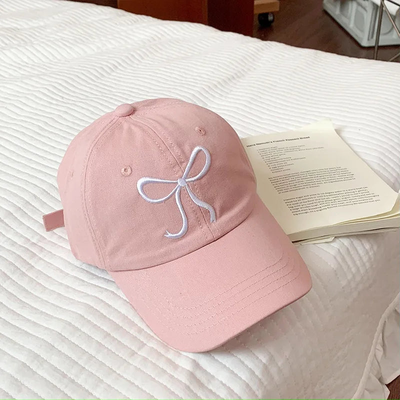 Pink Kawaii cap with a white bow design on a bed with an open book
