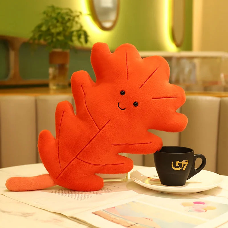 Red leaf-shaped kawaii plush toy on a table with a black cup and saucer.