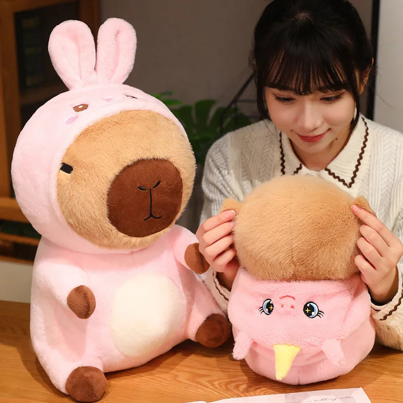 Person holding two kawaii plush toys resembling a pink and brown creature on a wooden surface.