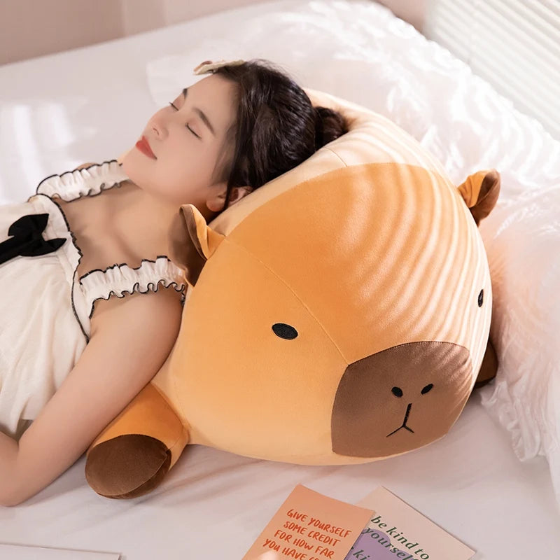 Person lying on a bed with a large kawaii plush cartoonish animal head pillow.