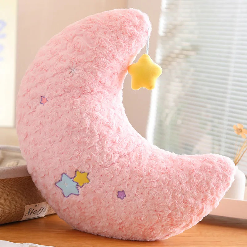 Pink crescent moon-shaped kawaii plush toy with star designs on a wooden surface.