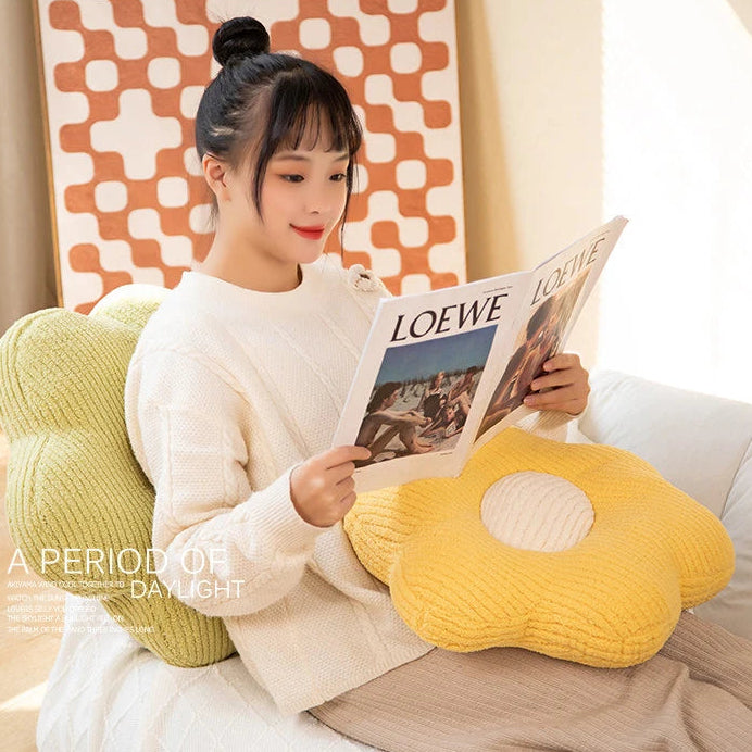 Woman reading a magazine on a yellow flower-shaped kawaii pillow with a colorful wall in the background