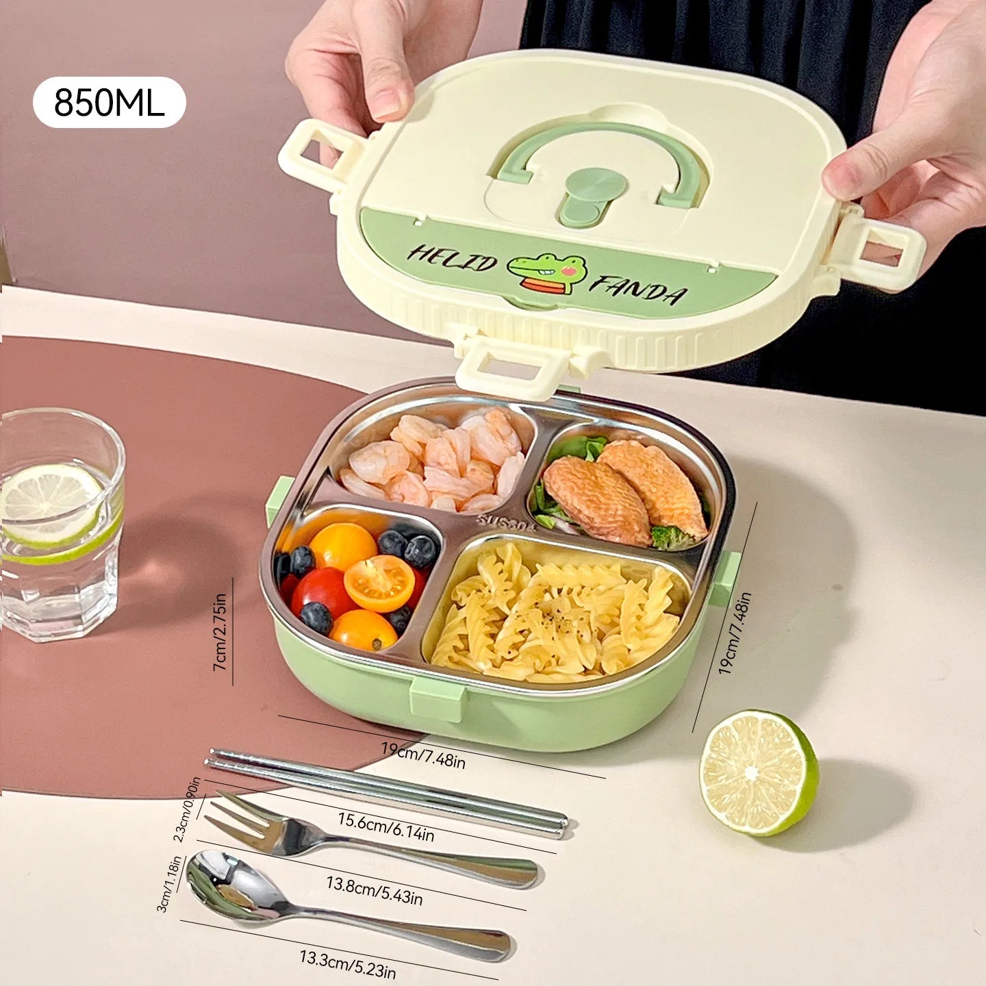 Green kawaii bento box with compartments filled with food, a glass of water, and cut lemon on a pink surface.