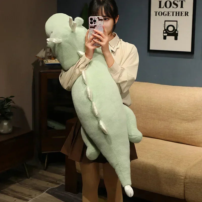 Person holding a large green kawaii plush toy in a room with a couch and framed picture on the wall.