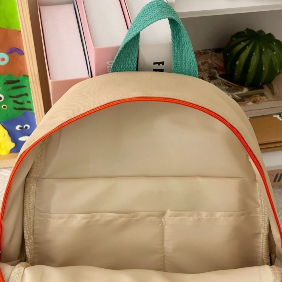 Kawaii beige backpack with orange trim on a shelf with books and a plant.