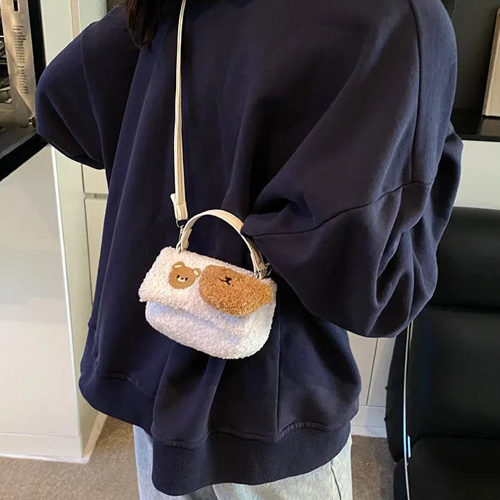 Person wearing a navy blue hoodie with a small white bag featuring a Kawaii teddy bear design.