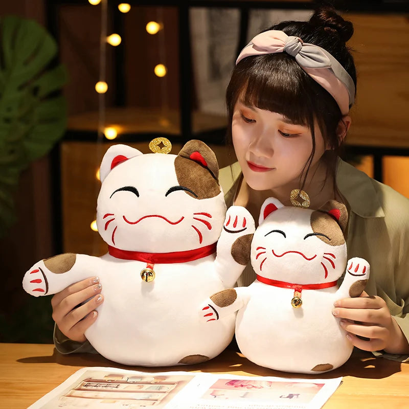 Person holding two Maneki Neko kawaii plush toys in a warm indoor setting.