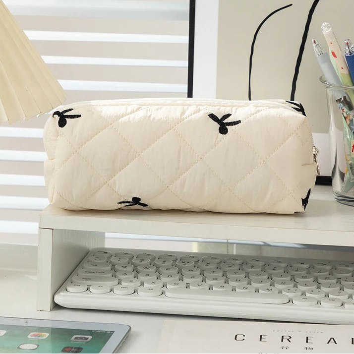 White quilted pouch with black butterfly kawaii designs on a desk with a keyboard and tablet.