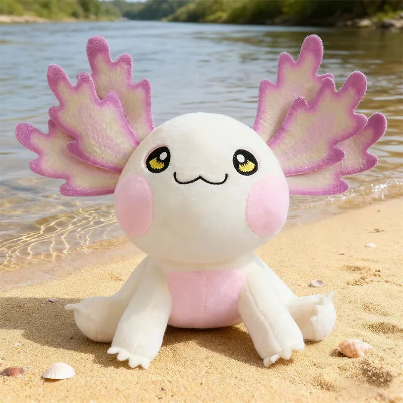 Plush kawaii axolotl toy on a sandy beach with water in the background