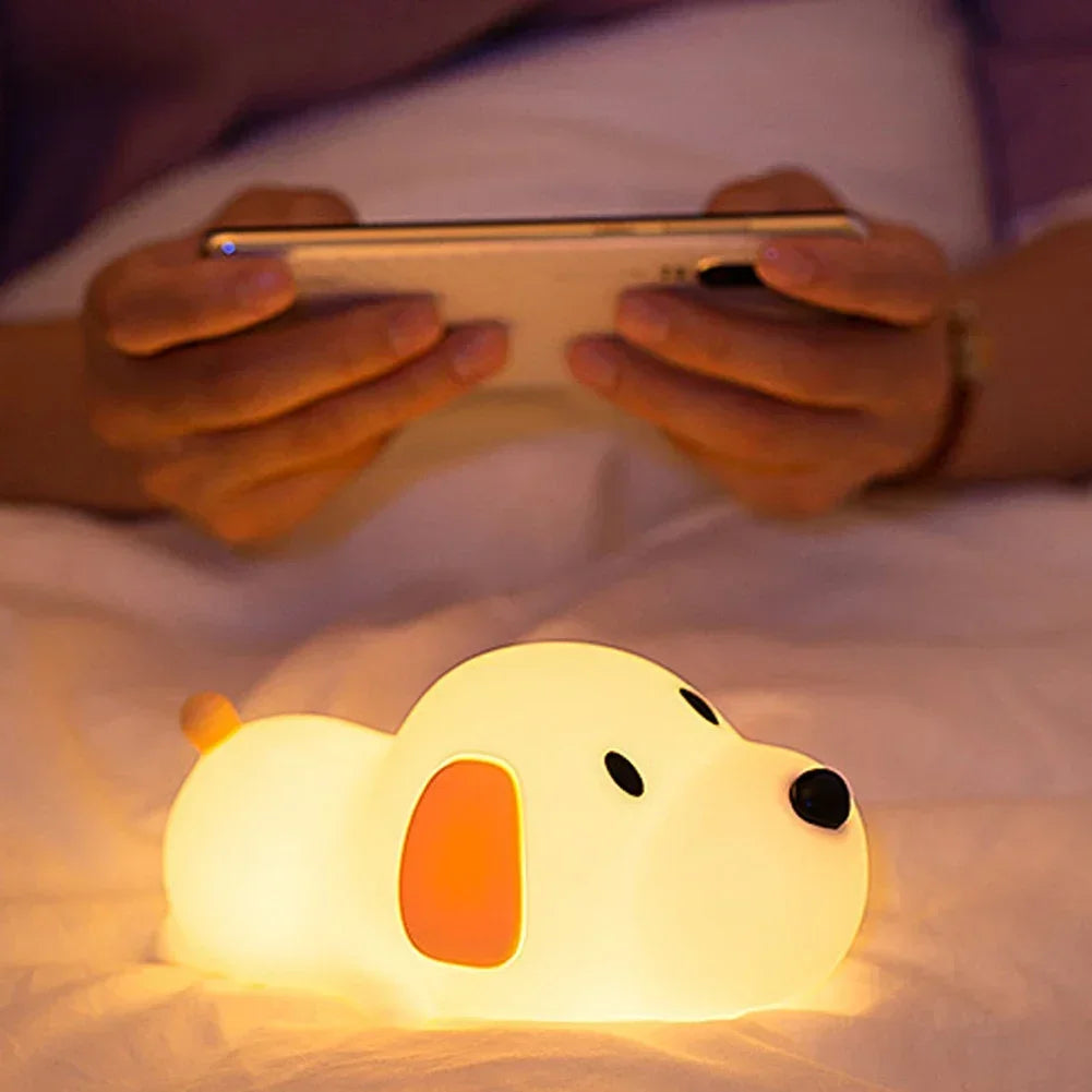 Person using a smartphone with a glowing dog-shaped kawaii night light on a bed.