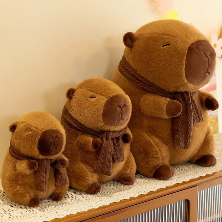 Three brown kawaii teddy bears of different sizes wearing scarves on a decorative surface.