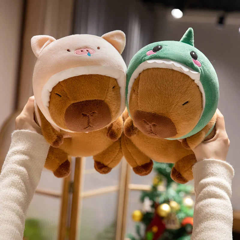 Two kawaii plush toys resembling bears with animal hats held by a person against a blurred indoor background.