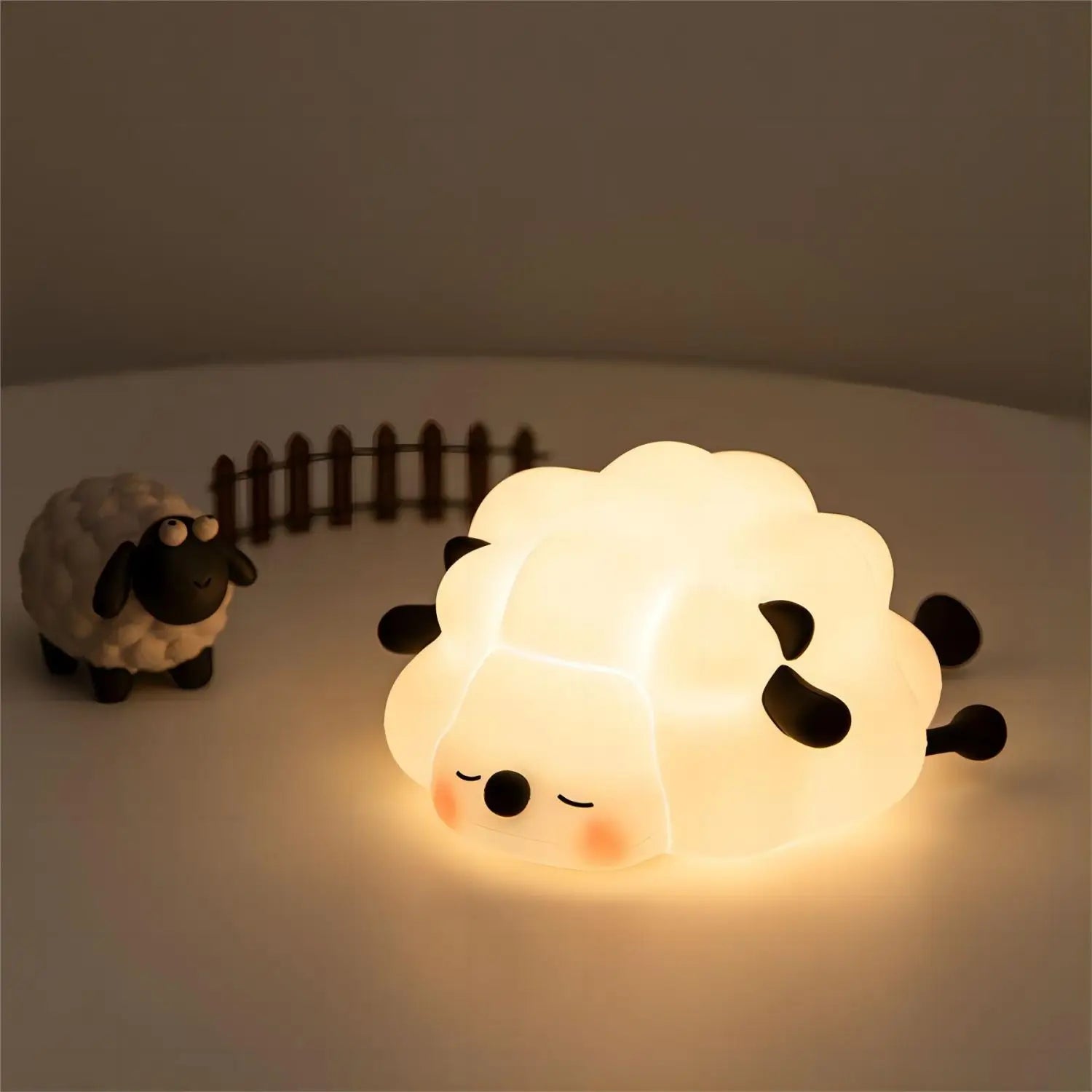 Kawaii sheep-shaped night light with a smaller sheep figure and wooden fence on a neutral background