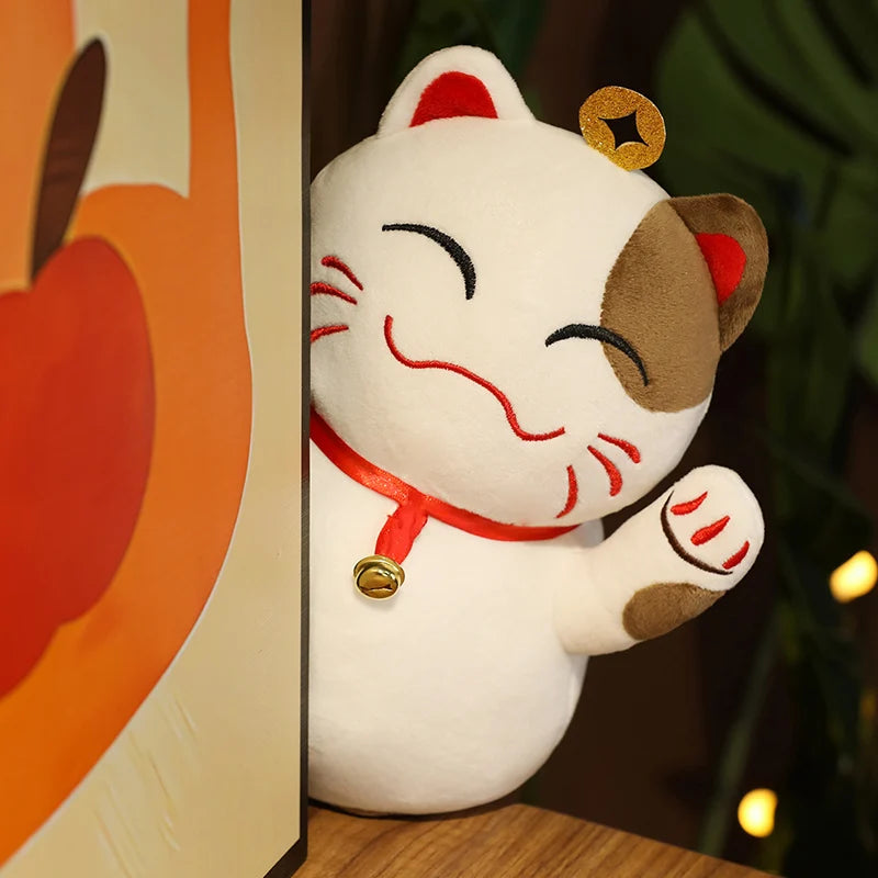 Kawaii plush toy of a cat with a red ribbon and bell, resembling a maneki-neko, in front of an orange background.