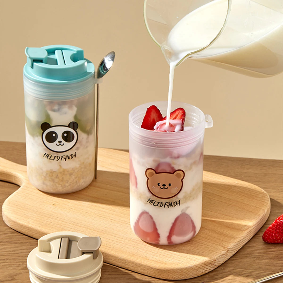 Transparent tumbler with Kawaii bear design being filled with milk and strawberries on a wooden surface.