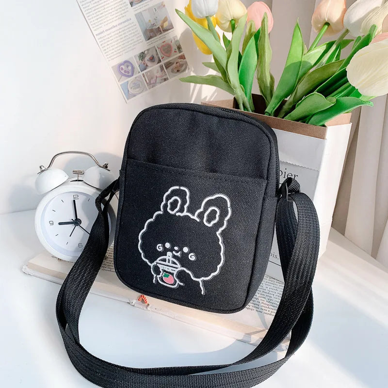 Black crossbody bag with a white embroidered Kawaii design on a surface with a clock and flowers.