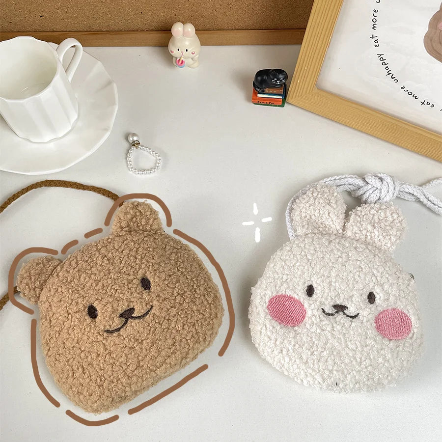 Two plush pouches shaped like a Kawaii bear and a rabbit on a white surface with a cup and saucer in the background.