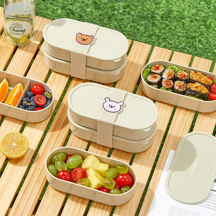 Two kawaii beige bento boxes with food on a wooden table outdoors.