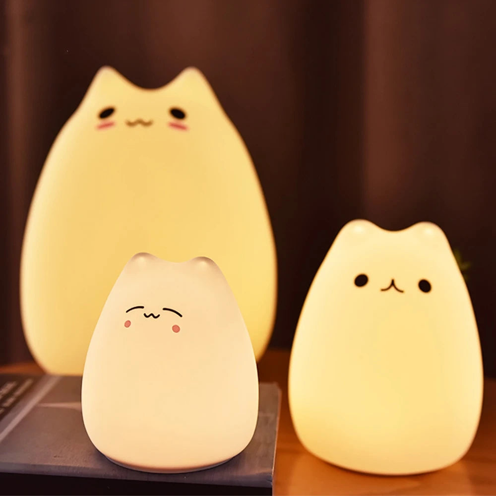 Three kawaii cat-shaped night lights on a wooden surface with a dark background
