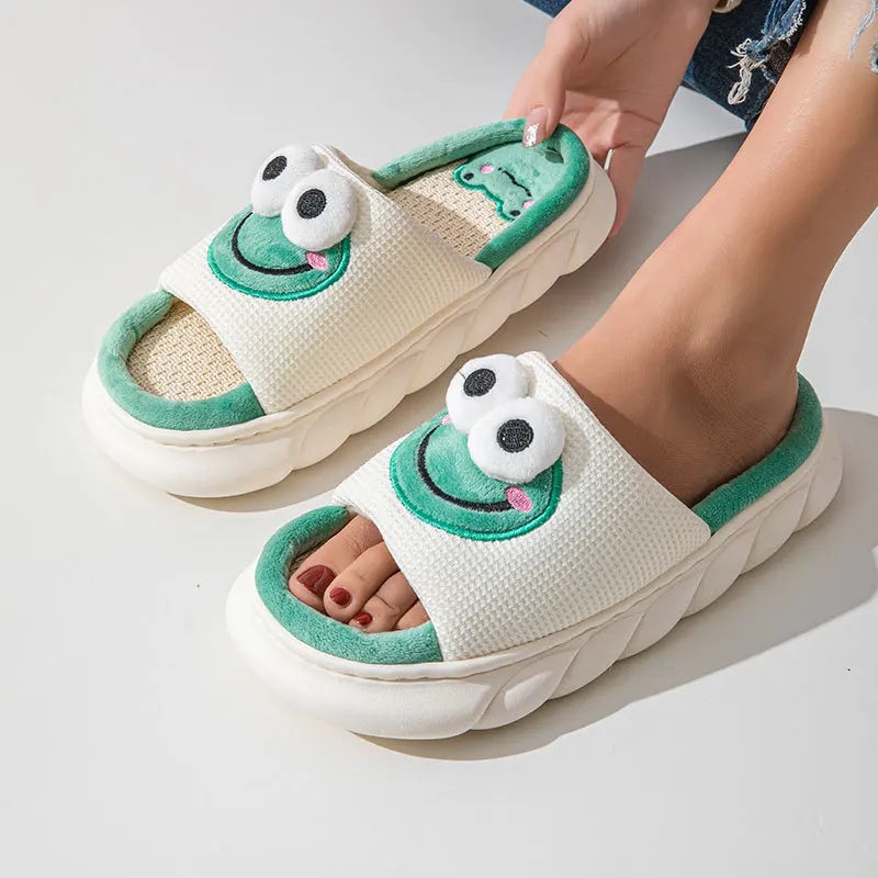 White slippers with green accents and kawaii cartoonish face design worn by a person on a light gray background