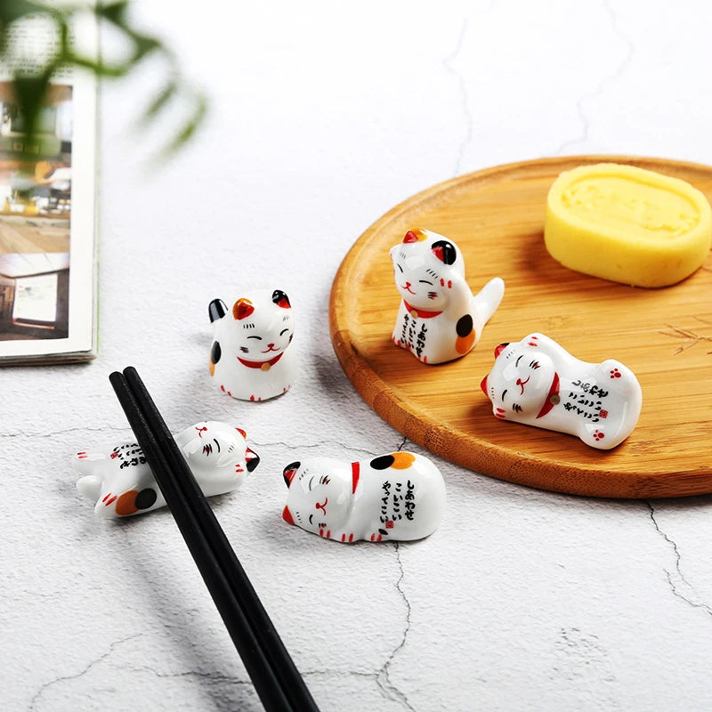 Set of small white kawaii cat figurines with red and black accents on a wooden plate with a yellow item.