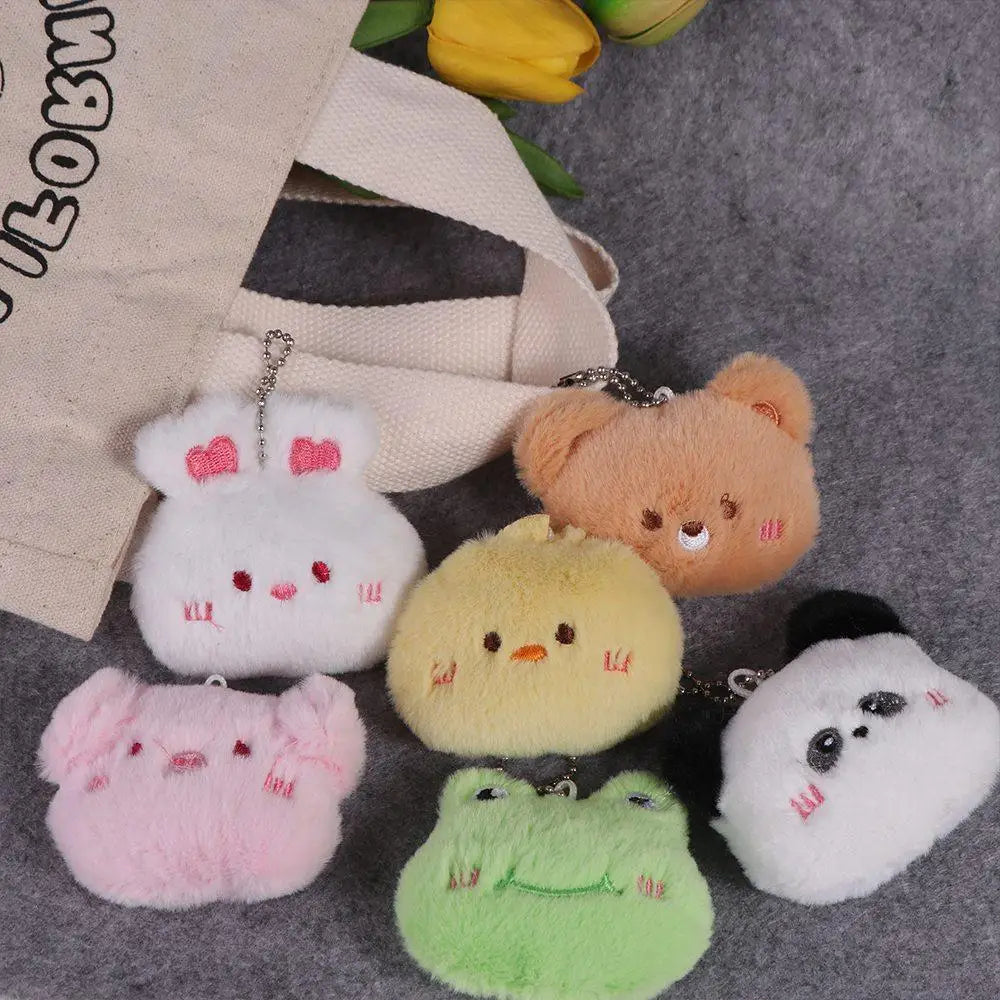 Set of plush kawaii animal keychains on a textured surface with a bag and flowers in the background.