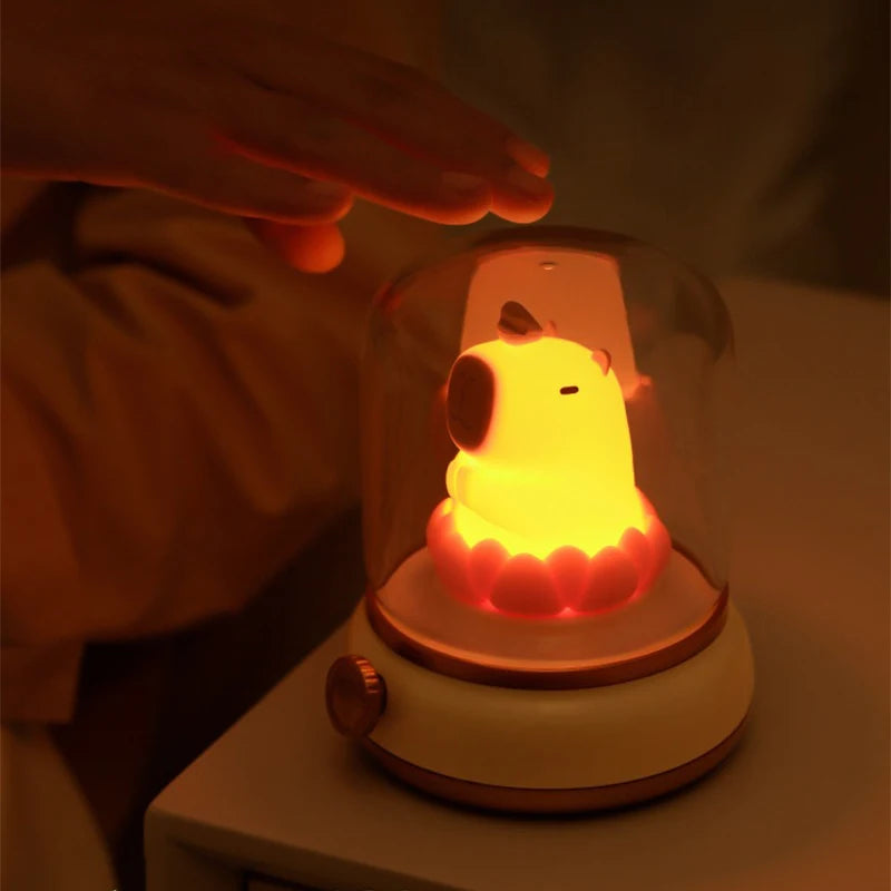 Glowing kawaii capybara night light under a glass dome with a hand reaching towards it.