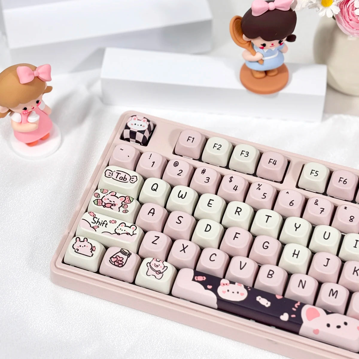 Keyboard with Kawaii keycaps on a white surface with small figurines in the background