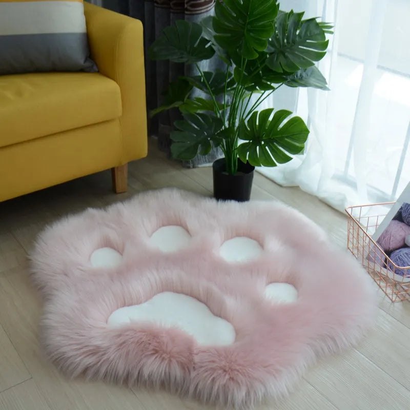 Pink kawaii fluffy cloud-shaped cushion on a light wooden floor with a yellow sofa and plant in the background.