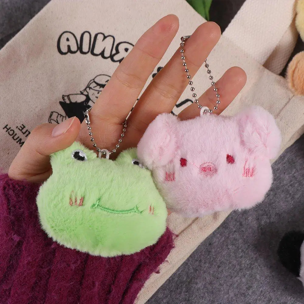 Two plush kawaii keychains, one green and one pink, held by a hand against a neutral background.