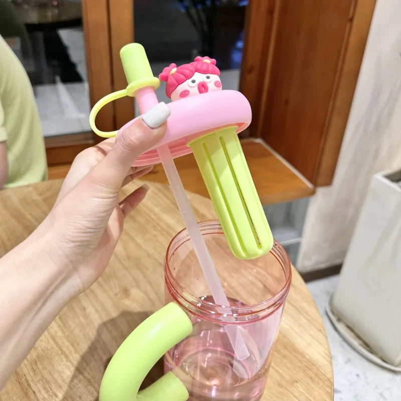 Kawaii pink and green cup with straw and handle held by a hand, blurred indoor background